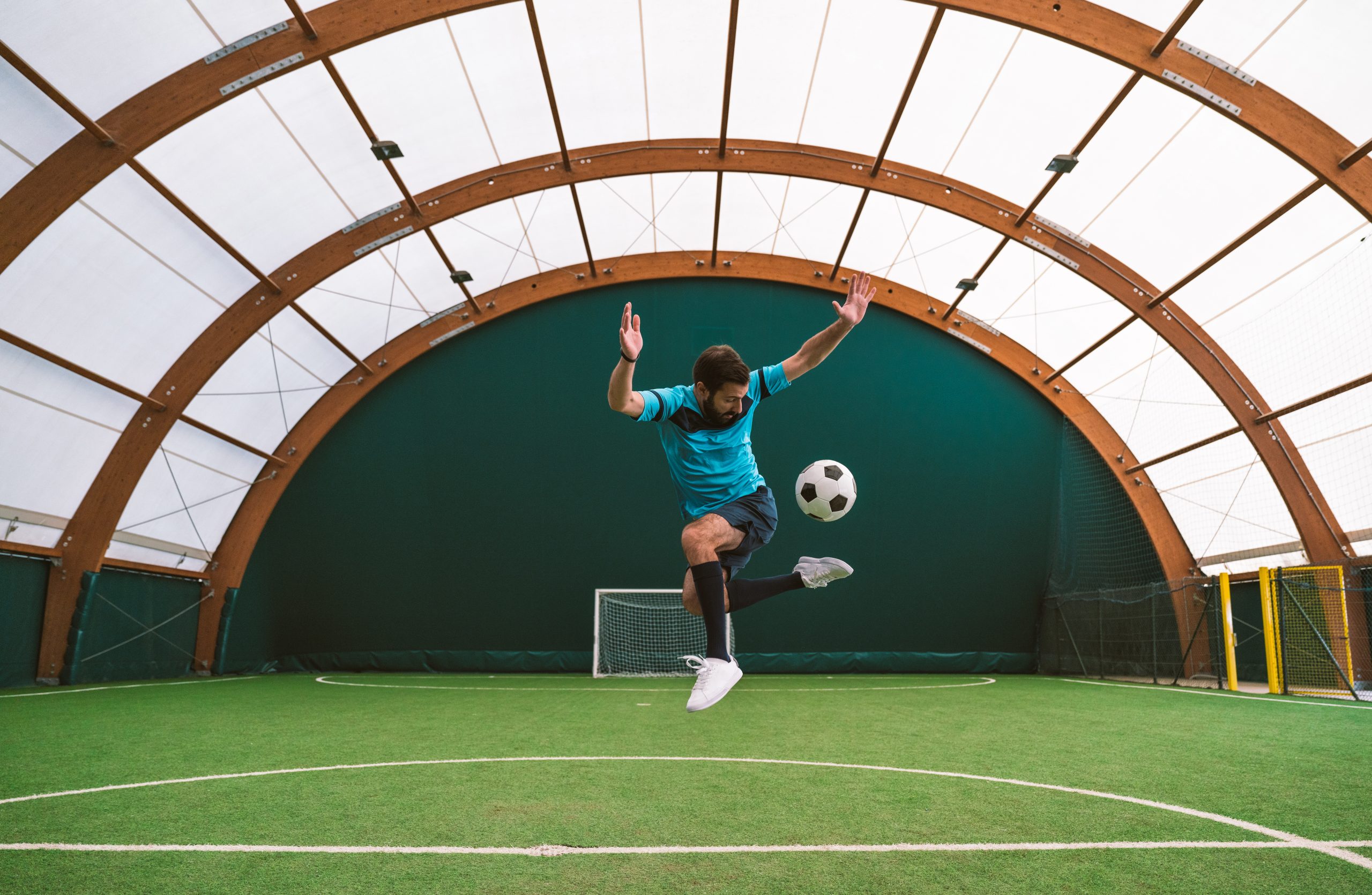 Fussballer kickt Ball in Sporthalle